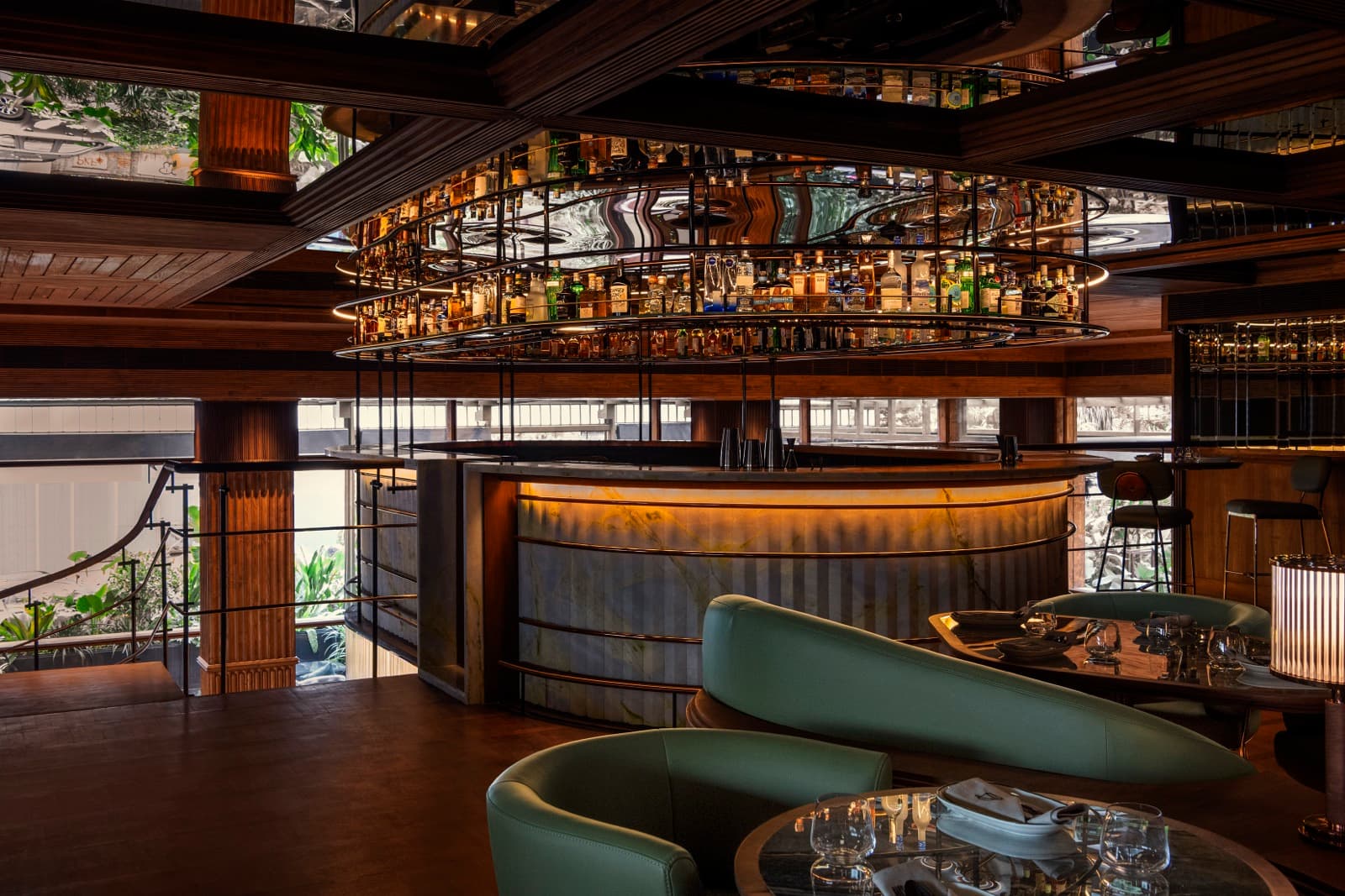 A wide-angle, architectural shot of the Muro Mezz upstairs bar in Bengaluru. The space features warm, dramatic lighting, a circular bar with glowing amber panels, mirrored ceilings, and sophisticated dark wood interiors with plush seating.