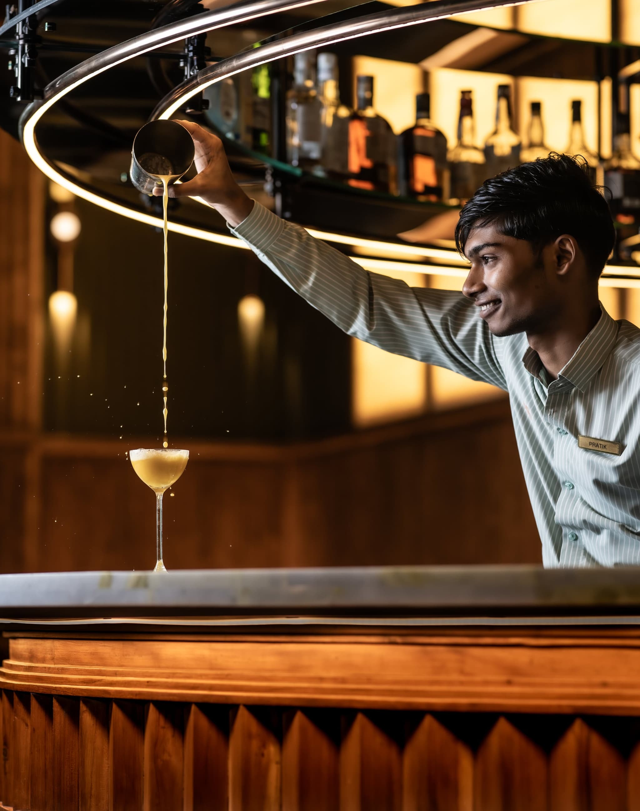 A MURO bartender pouring a cocktail at the island bar under hanging brass lights