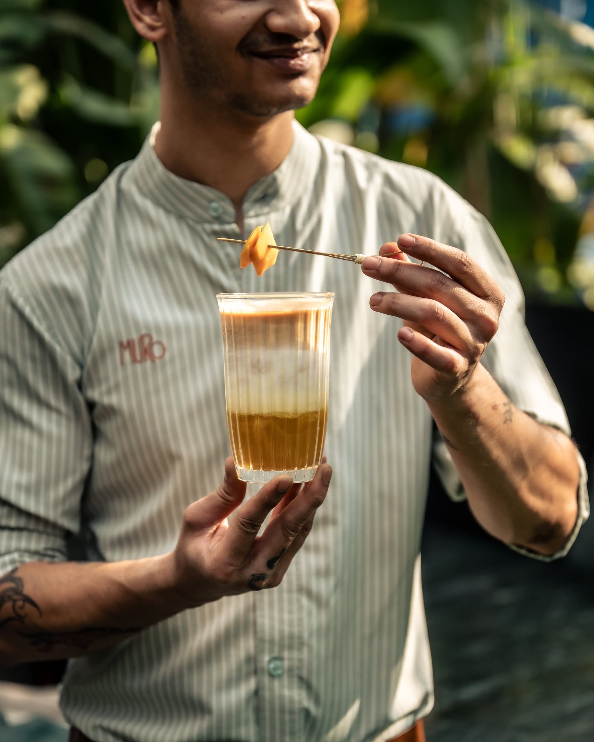 A MURO server holding a layered cocktail with a fruit garnish